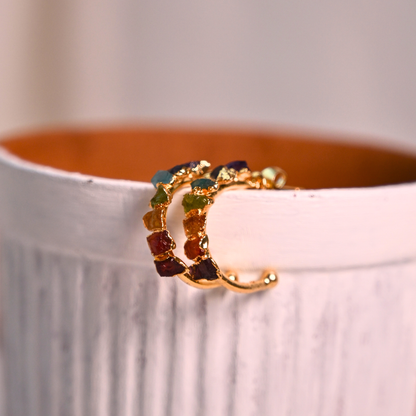 Gold-plated natural stone chakra hoop earrings displayed along the edge of a ceramic vessel.