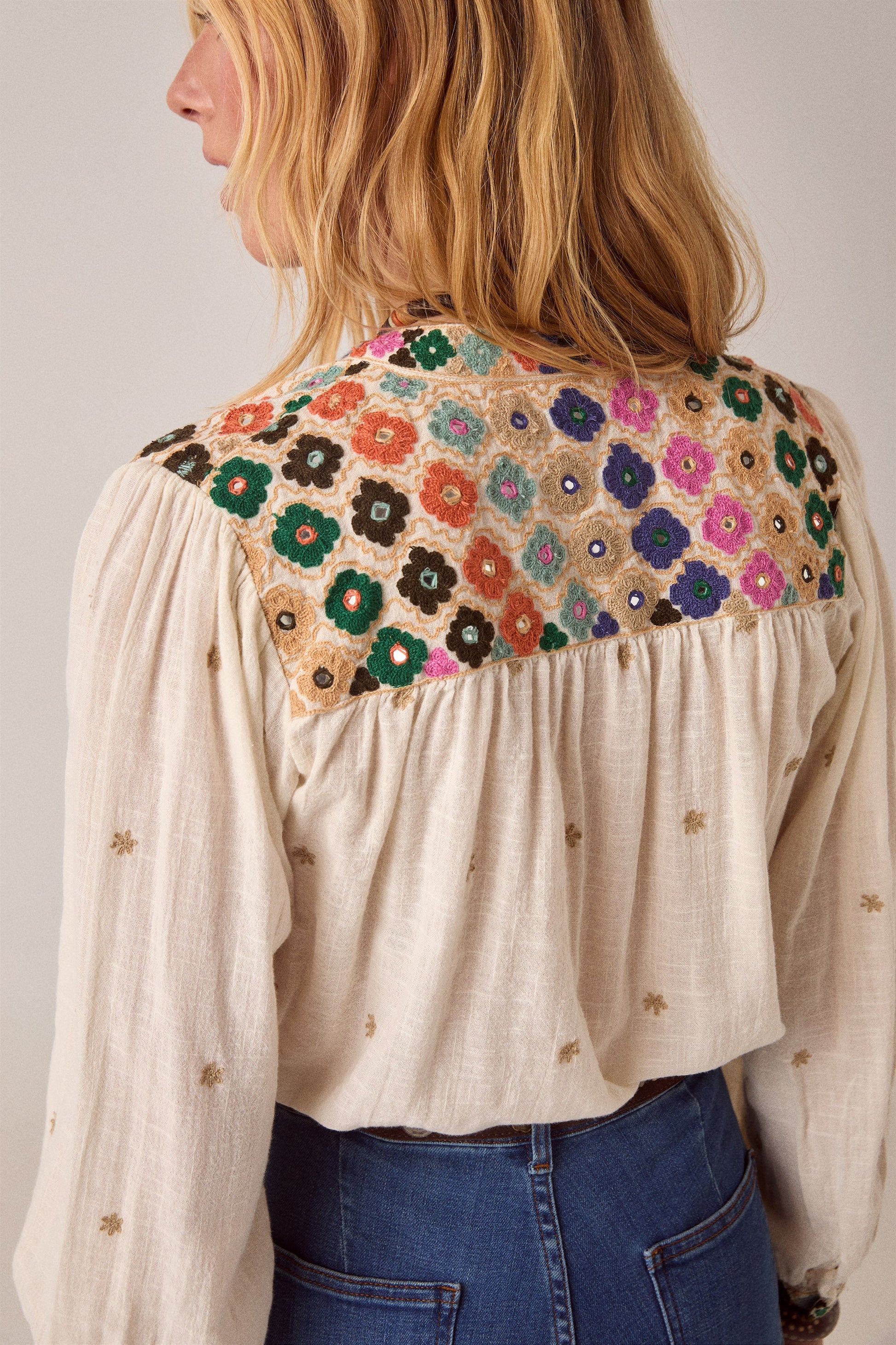 Back view of the Cleo blouse showcasing an intricately embroidered floral yoke in vibrant colors against a soft off-white fabric.