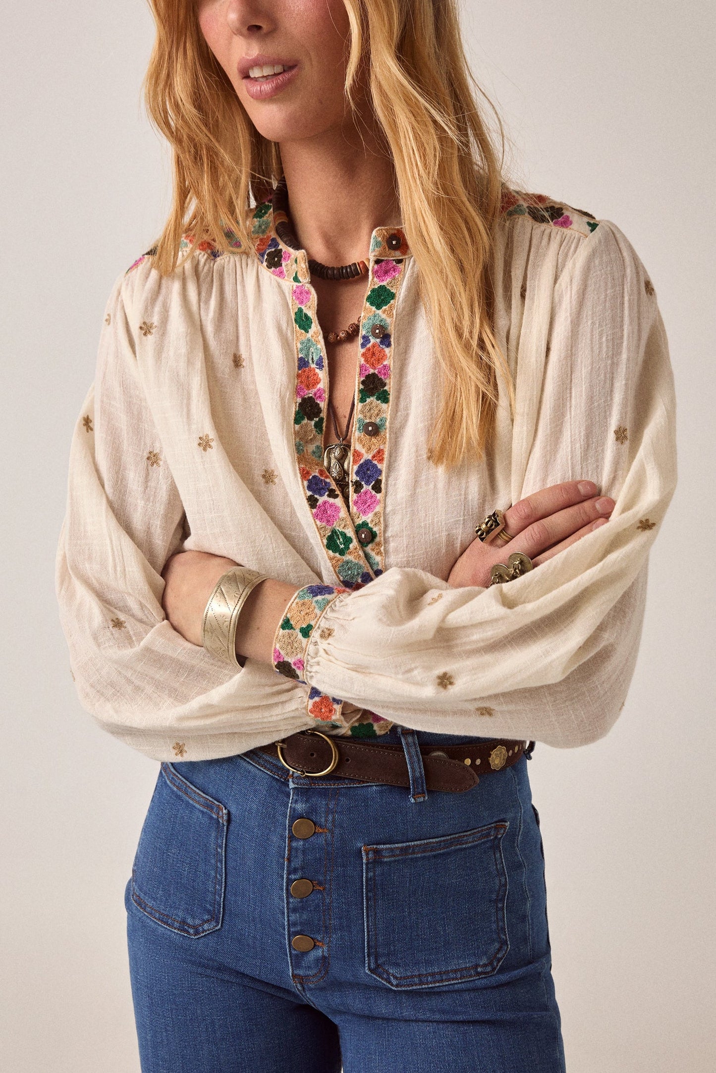 Close-up of the Cleo blouse showcasing colorful embroidered floral trim along the front placket and cuffs with delicate embroidered motifs throughout the fabric.