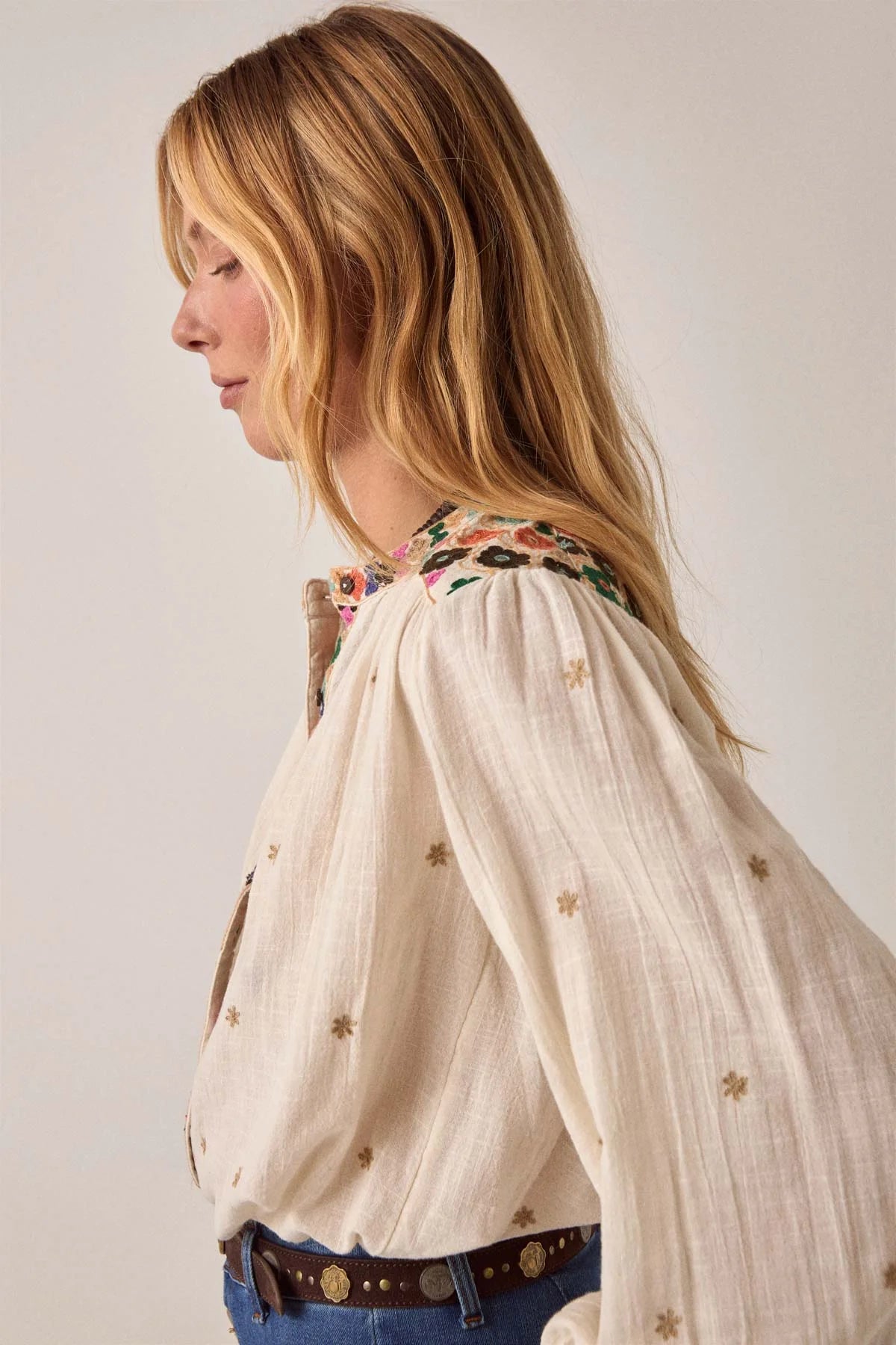 Side profile of the Cleo blouse in off-white featuring gathered shoulders, colorful embroidery along the yoke, and an airy relaxed silhouette.