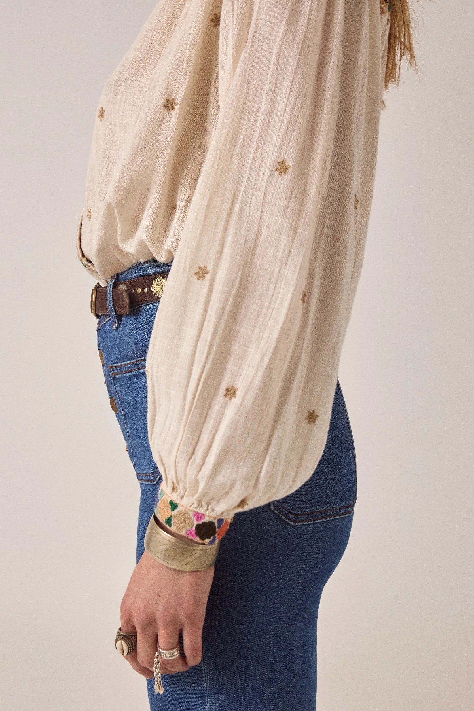 Side detail of the Cleo blouse highlighting the voluminous long sleeve, embroidered cuff, and soft textured off-white fabric with small embroidered motifs.