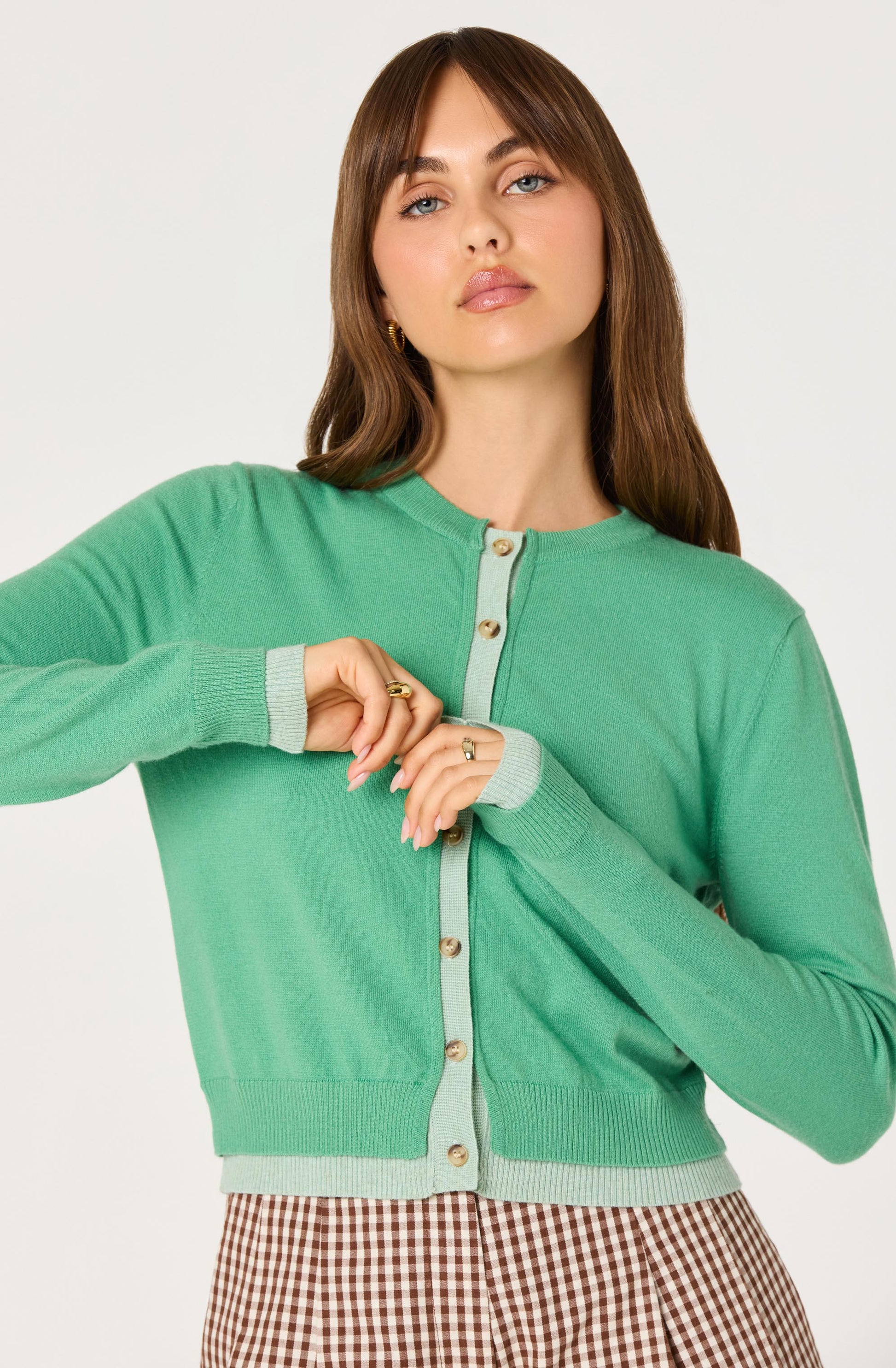 Close-up of the Clovis Color Block Faux Layered Cardigan showing the green knit, light contrast placket, round neckline, and button-front closure.