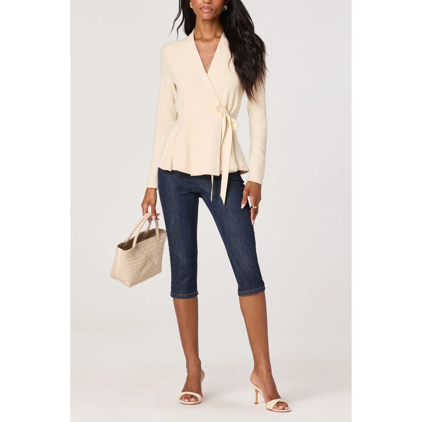 Model wearing the Dayna cream knit wrap top with dark denim capri jeans, neutral heels, and a woven handbag
