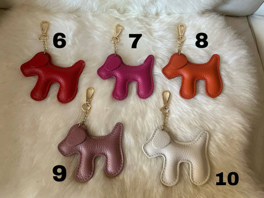 Dog-shaped genuine leather keychains displayed with numbered color options 6 through 10, including red, fuchsia, orange, mauve, and cream finishes.