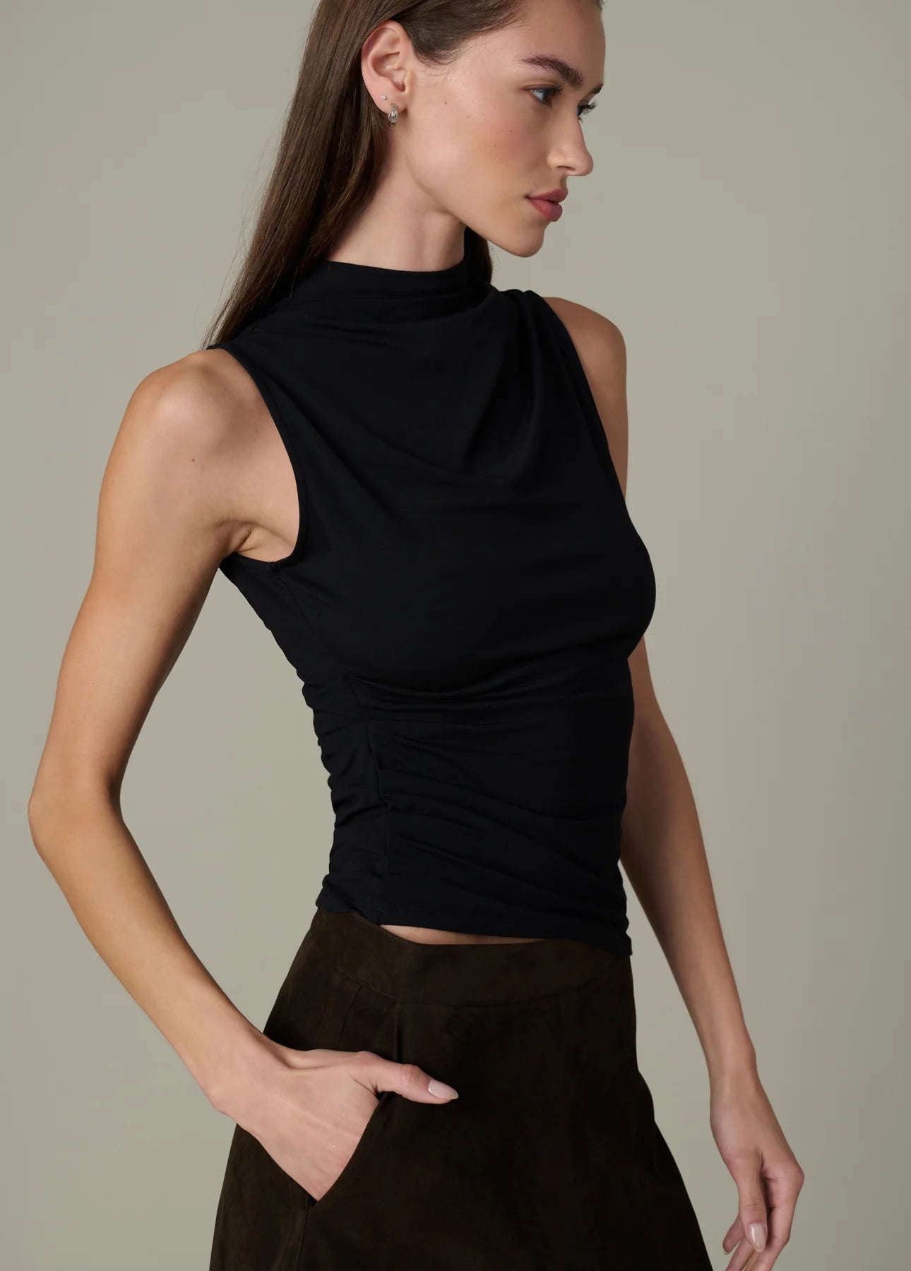 Model wearing the black Dove Top with an asymmetric draped neckline and standing collar, styled with a brown midi skirt.