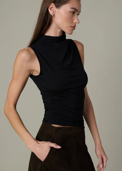 Model wearing the black Dove Top with an asymmetric draped neckline and standing collar, styled with a brown midi skirt.