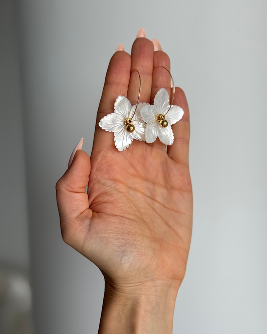 Hand holding FLOWER CHILD mother-of-pearl flower hoop earrings against a neutral background