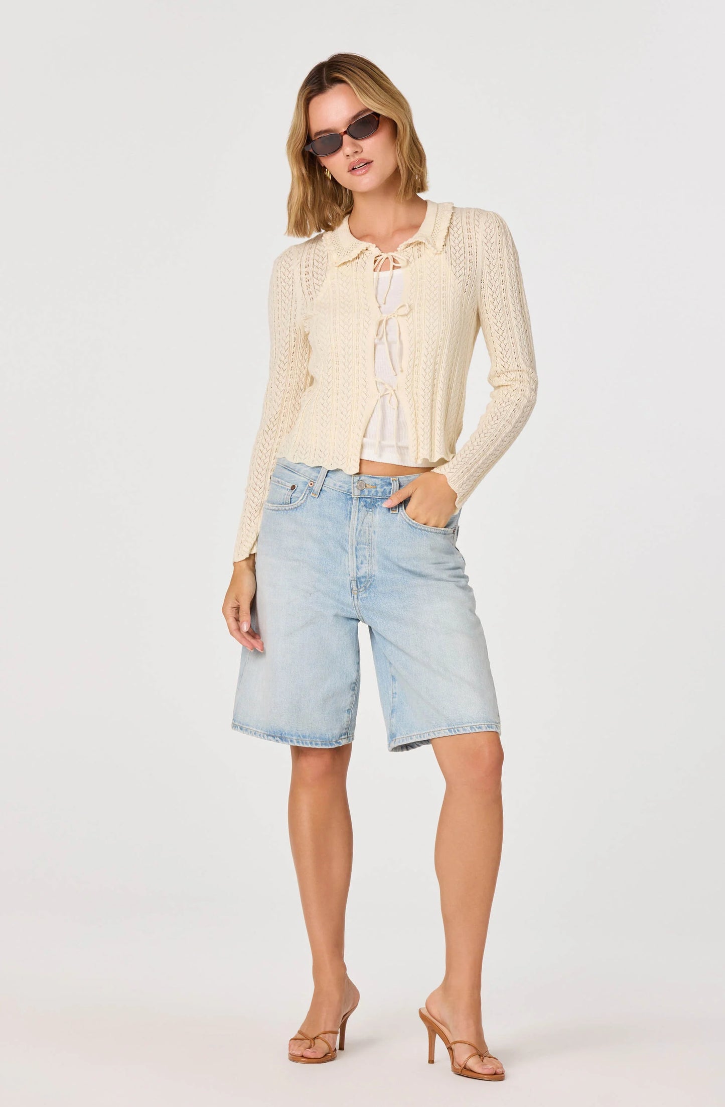 Model styling the cream Fannie Cardigan layered over a white top with denim shorts and sunglasses for a casual chic outfit.