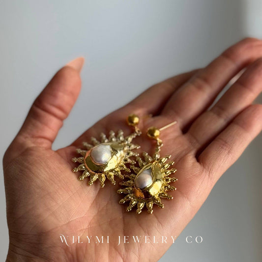 Close-up of Fire Pearl Statement Earrings with ornate gold-tone frames and pearl accents resting on hand
