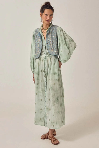 Model wearing the Freya Dress in Mineral Waves in jade cotton voile with tie-dye and paisley print, styled with a blue embroidered vest and sandals.