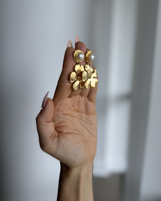 Full Bloom freshwater pearl drop earrings held up by hand, showing the dimensional gold floral design.