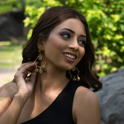 Model wearing rose quartz, citrine, and amethyst dangle earrings with a black sleeveless top outdoors.