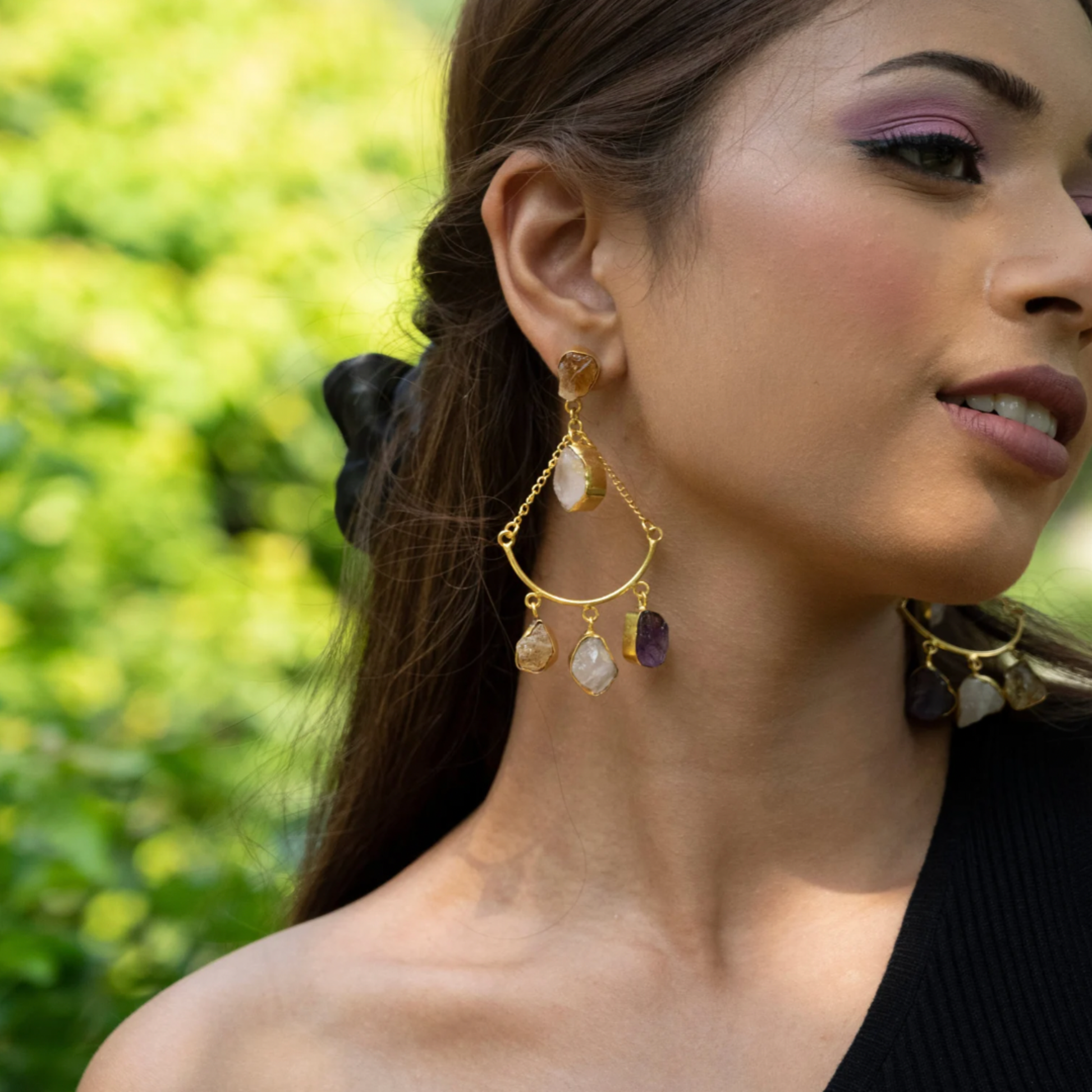 Side view of a model wearing the rose quartz, citrine, and amethyst dangle earring against a green outdoor setting.