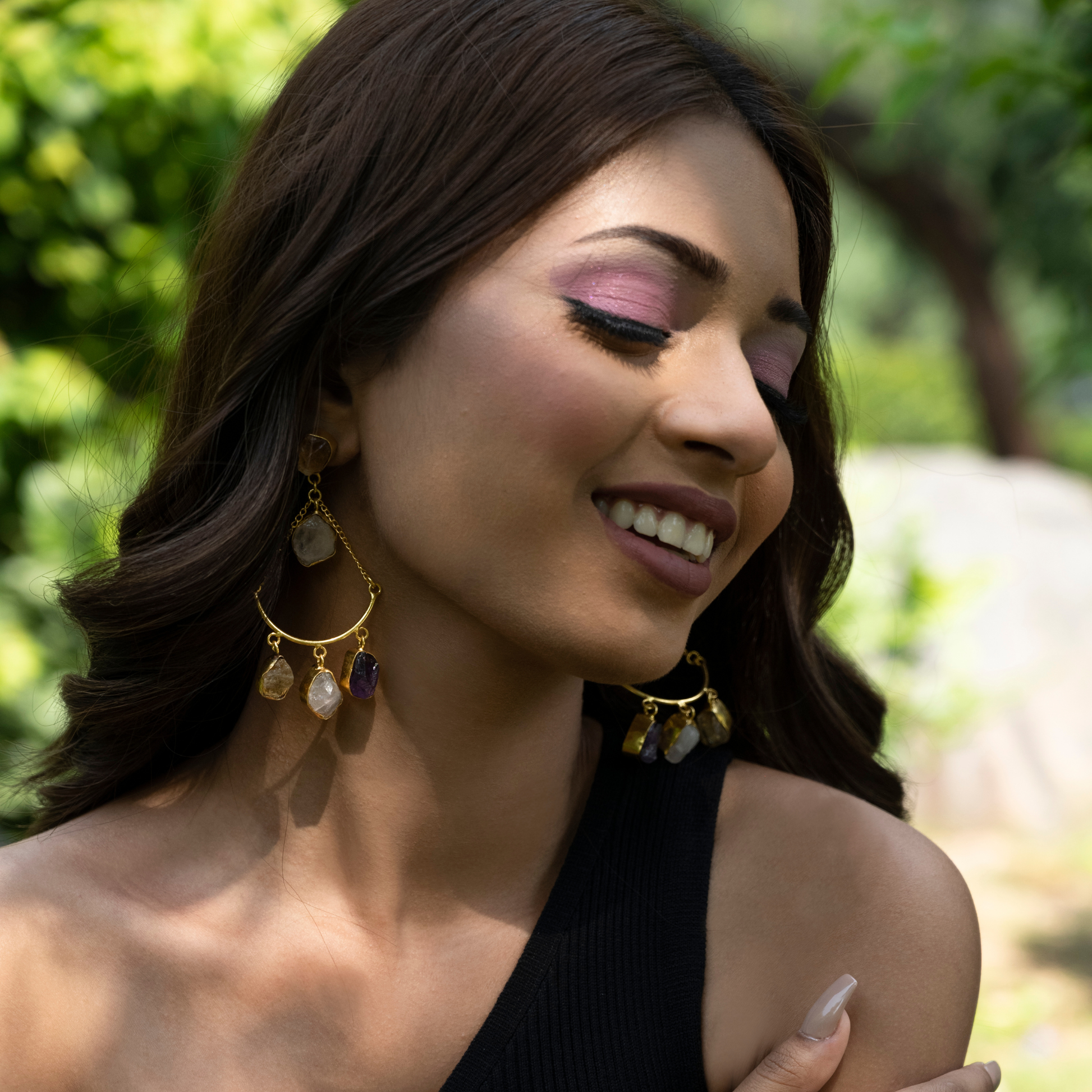 Smiling model wearing gold-plated rose quartz, citrine, and amethyst dangle earrings with a black top.