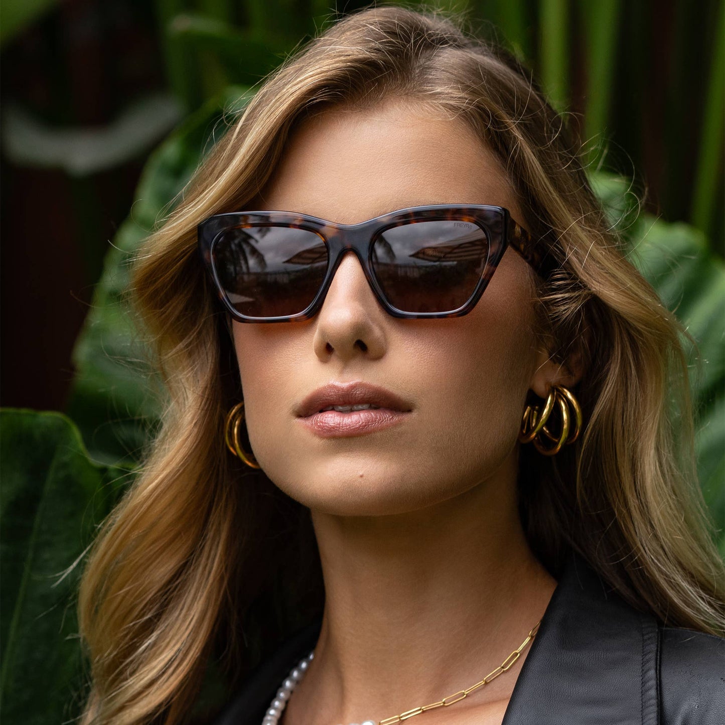 Model wearing Gia tortoise acetate cat-eye sunglasses with brown lenses in an outdoor setting.