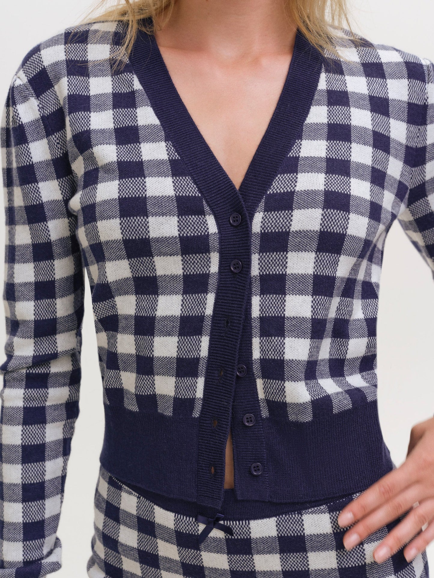 Close-up detail of the navy and white gingham knit cardigan featuring a V-neckline, navy ribbed trim, button-front closure, and soft textured knit fabric.