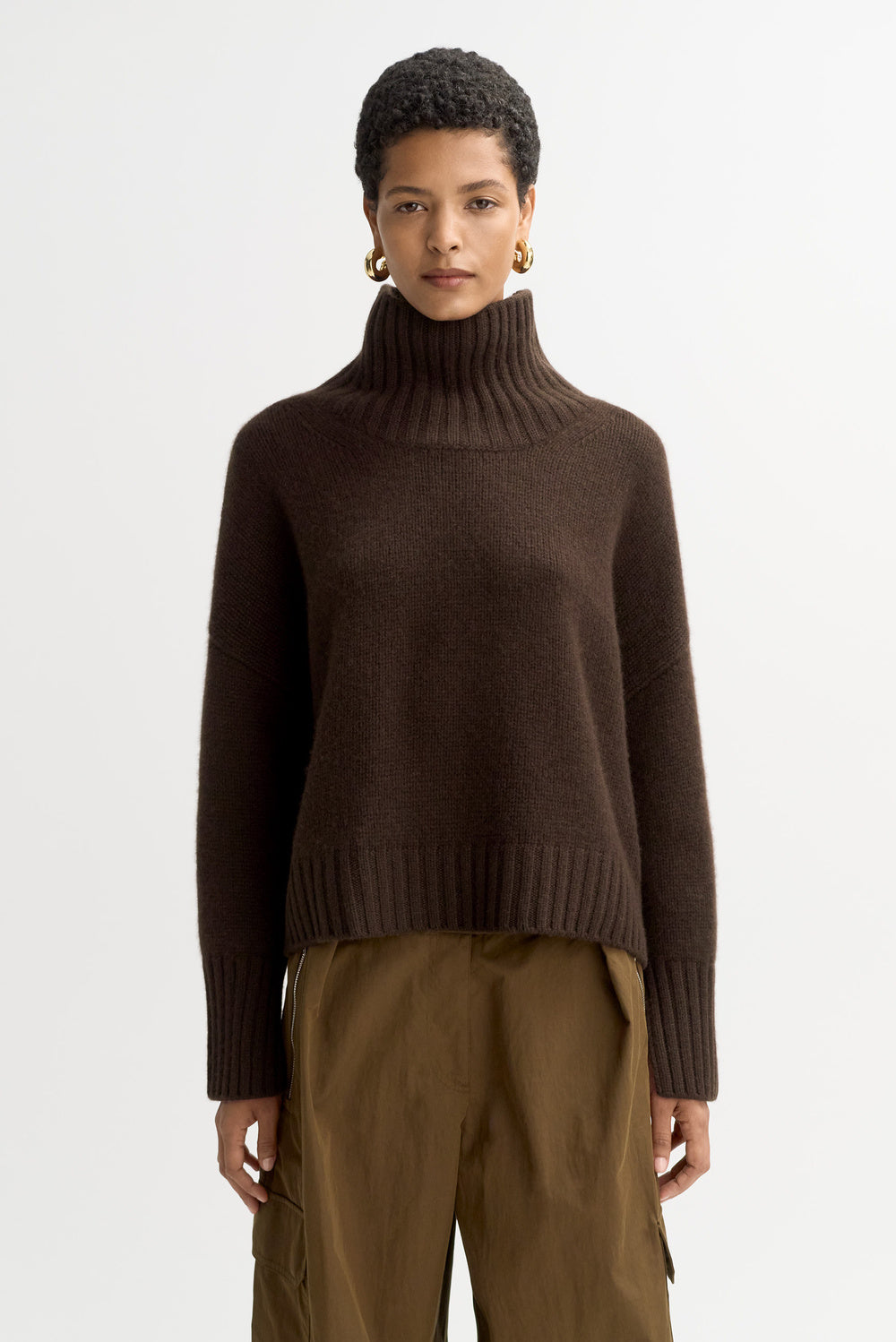 Model wearing the Girlfriend Turtleneck in mocha cashmere with olive trousers, shown from the front.
