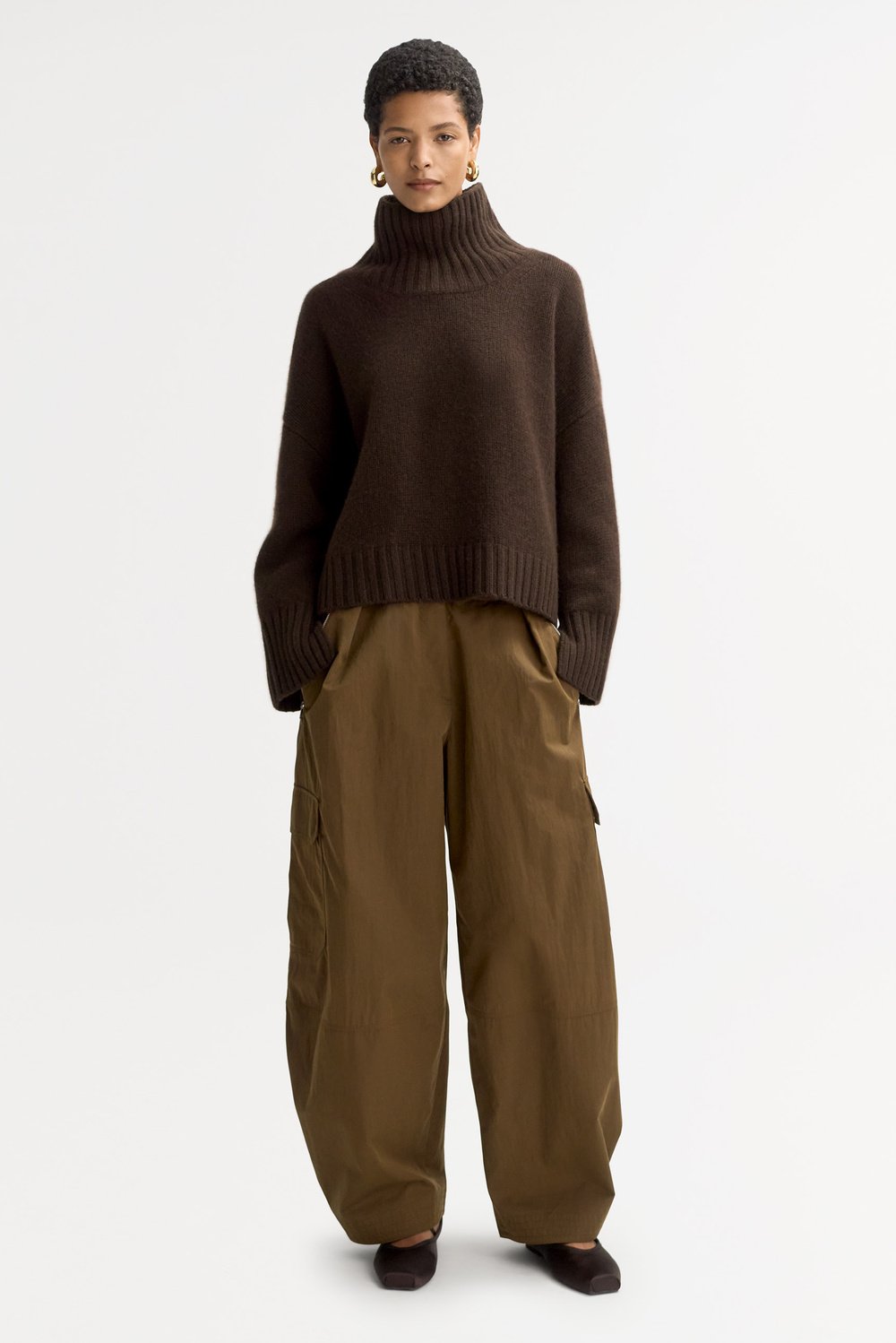 Full-length view of a model styling the mocha Girlfriend Turtleneck with relaxed olive trousers.
