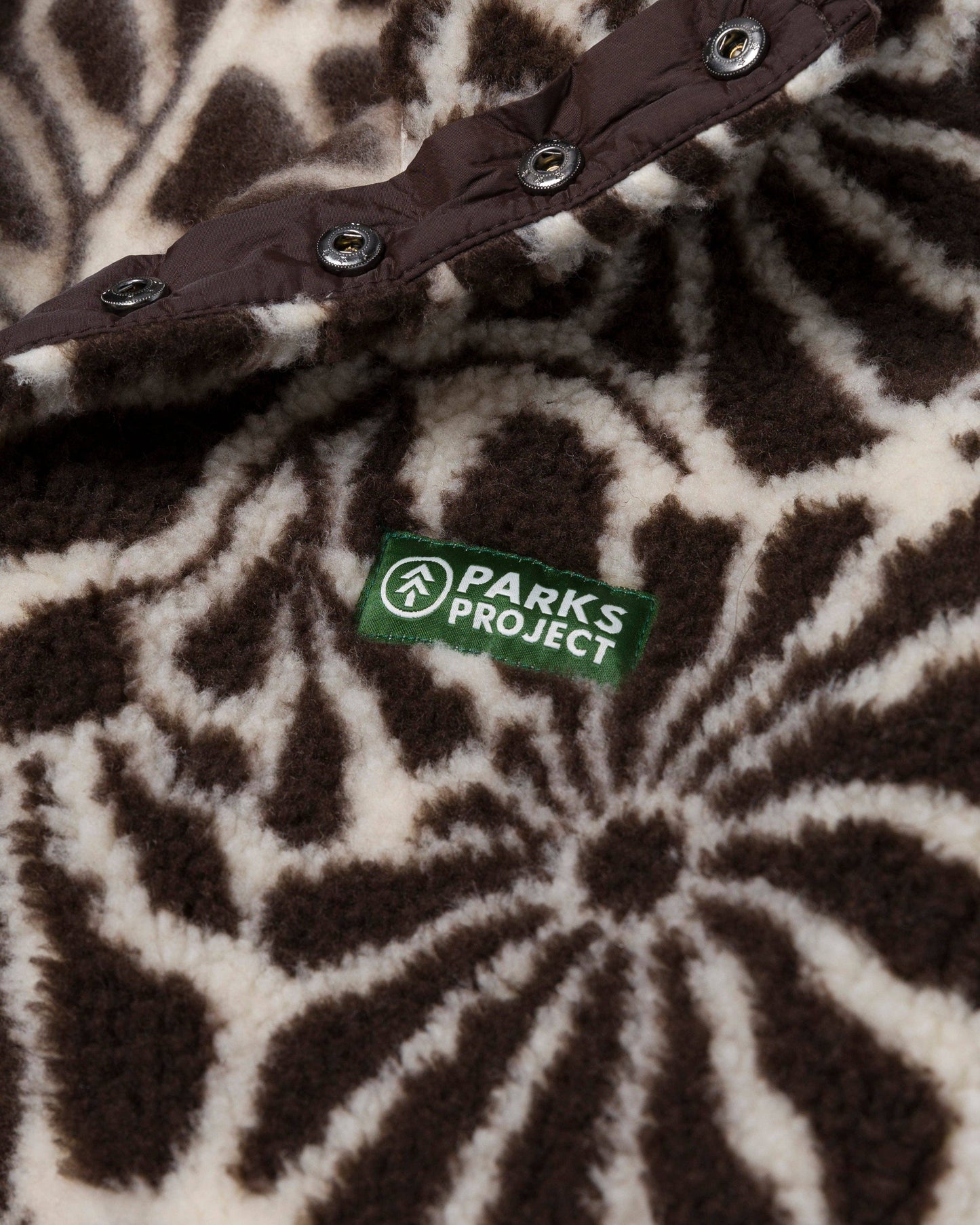 Close-up of the brown and natural floral fleece texture with its recycled-material certification label and snap detail.