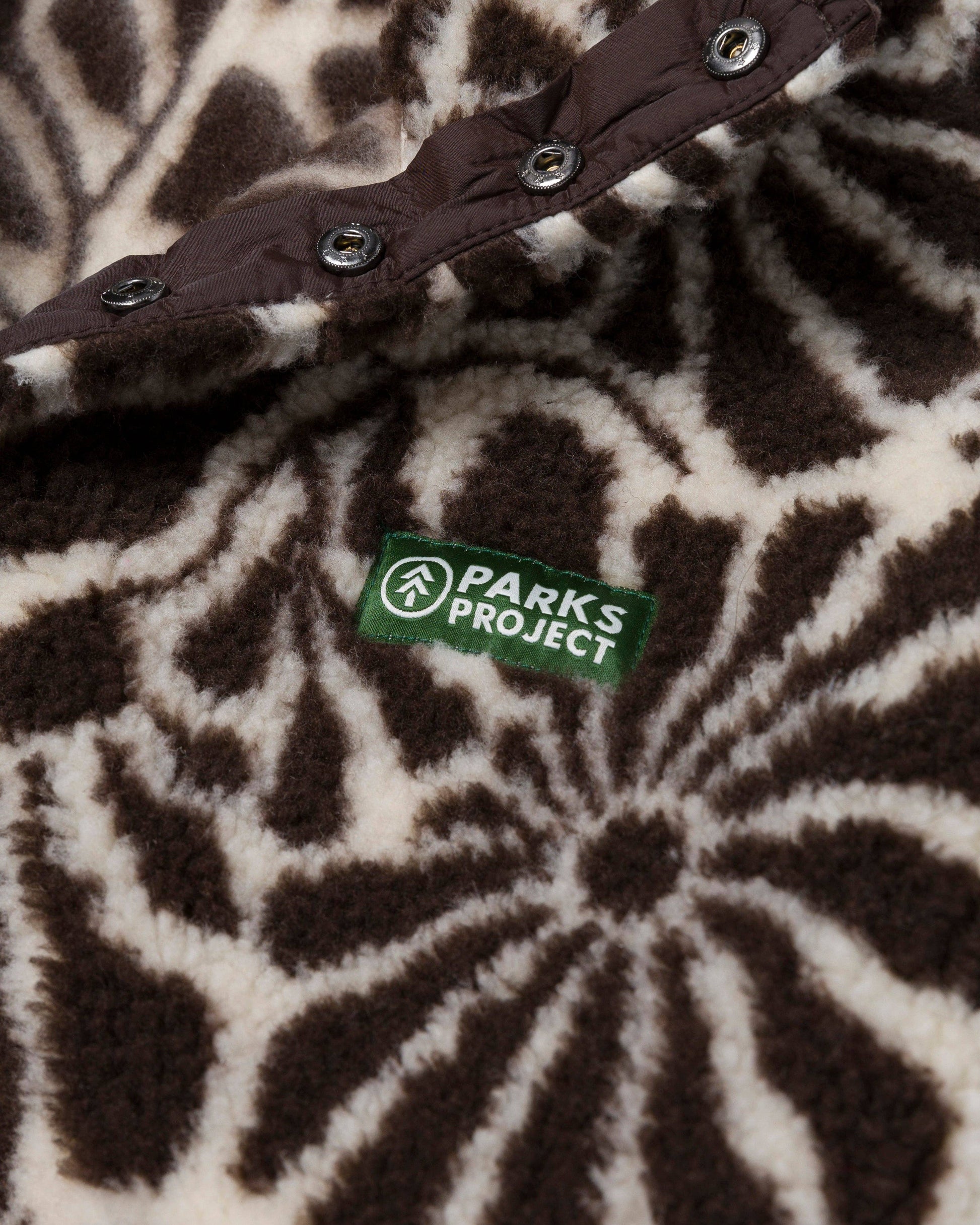 Close-up of the brown and natural floral fleece texture with its recycled-material certification label and snap detail.
