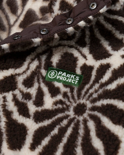 Close-up of the brown and natural floral fleece texture with its recycled-material certification label and snap detail.