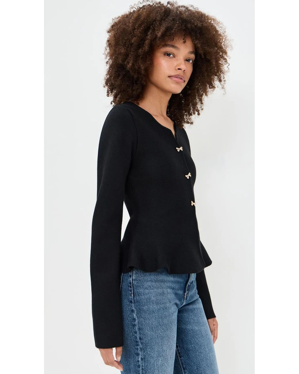 Side view of the black Idah Cardigan with gold-tone bow buttons, long sleeves, and a peplum hem.