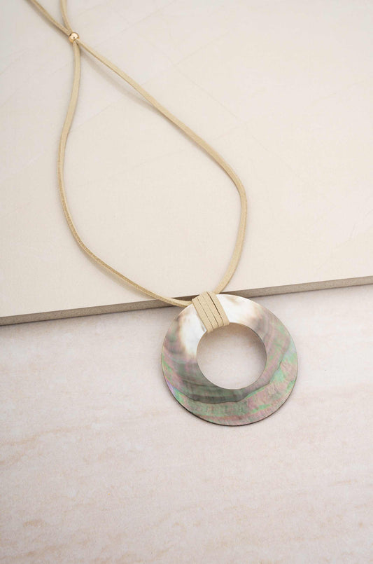 Iridescent shell circle pendant necklace with suede cord displayed on a neutral background