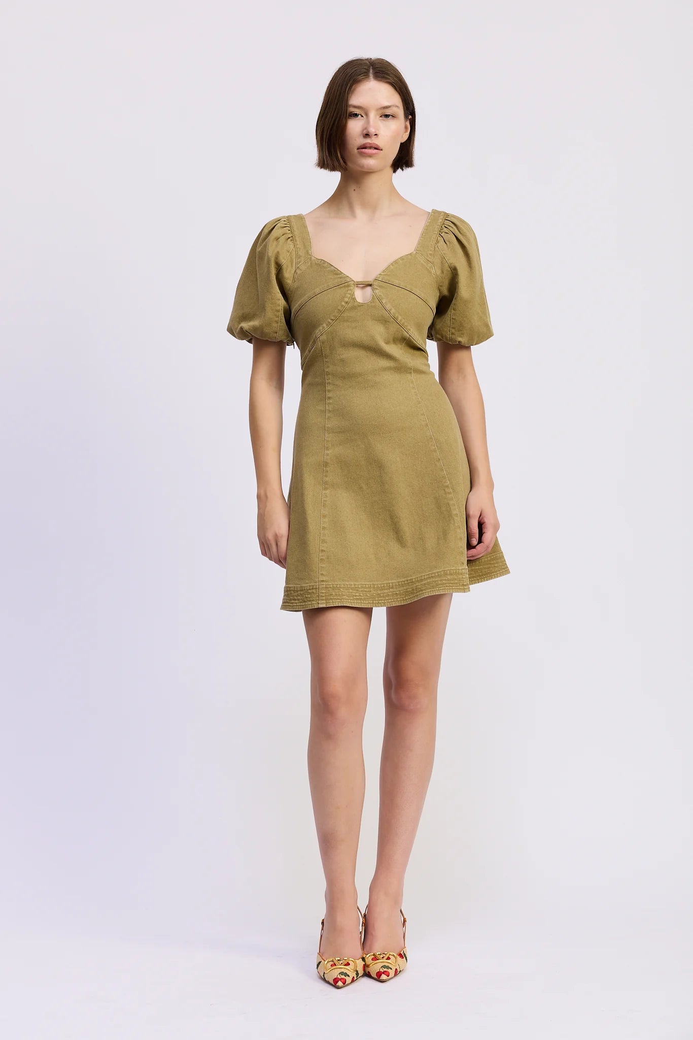 Model wearing the Isabelle Mini Dress in olive green featuring a sweetheart neckline with front cut-out detail, puff sleeves, fitted bodice, and flared A-line mini skirt.