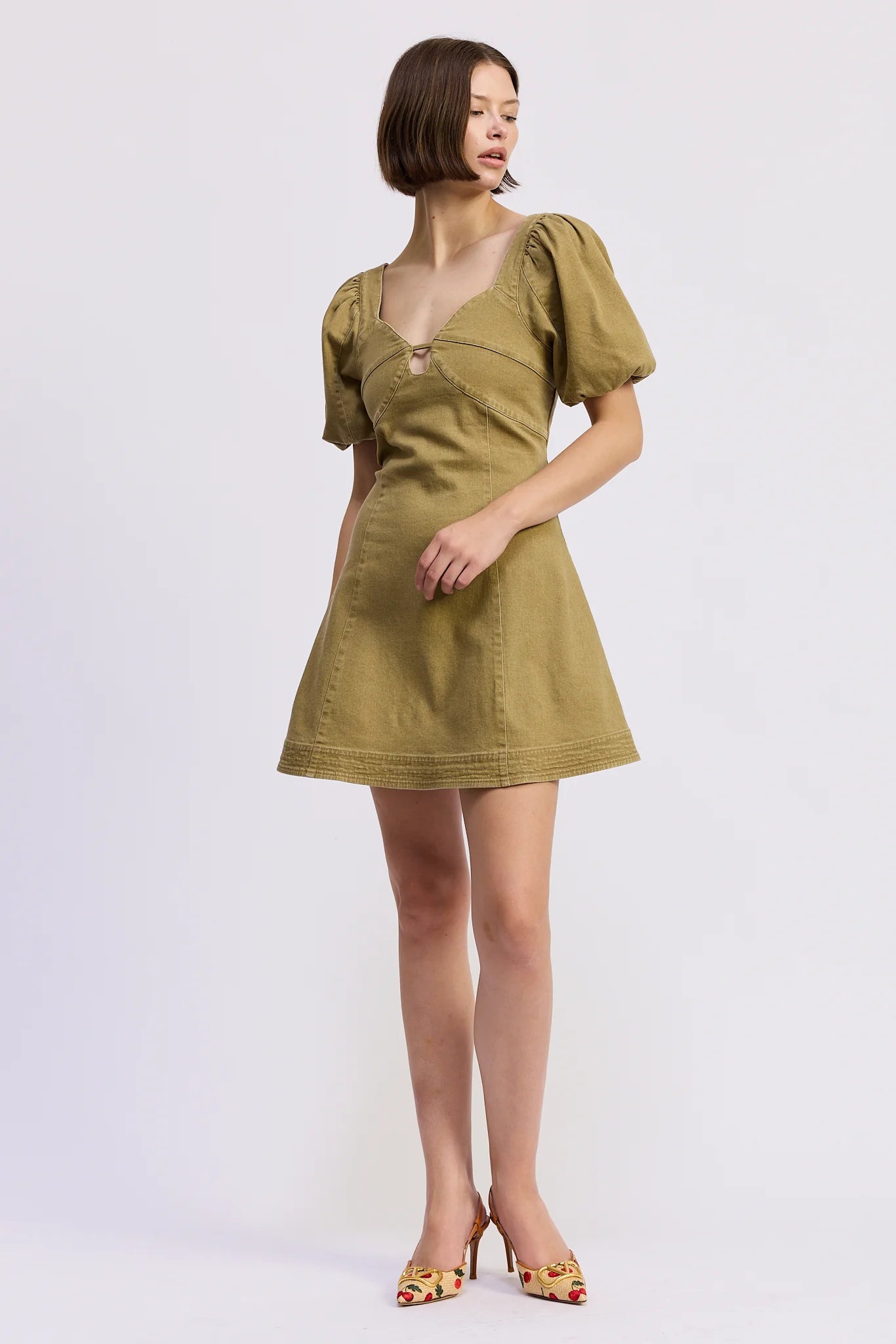 Side front view of the Isabelle Mini Dress in olive green featuring a structured bodice, subtle front cut-out, puff sleeves, and feminine A-line shape.