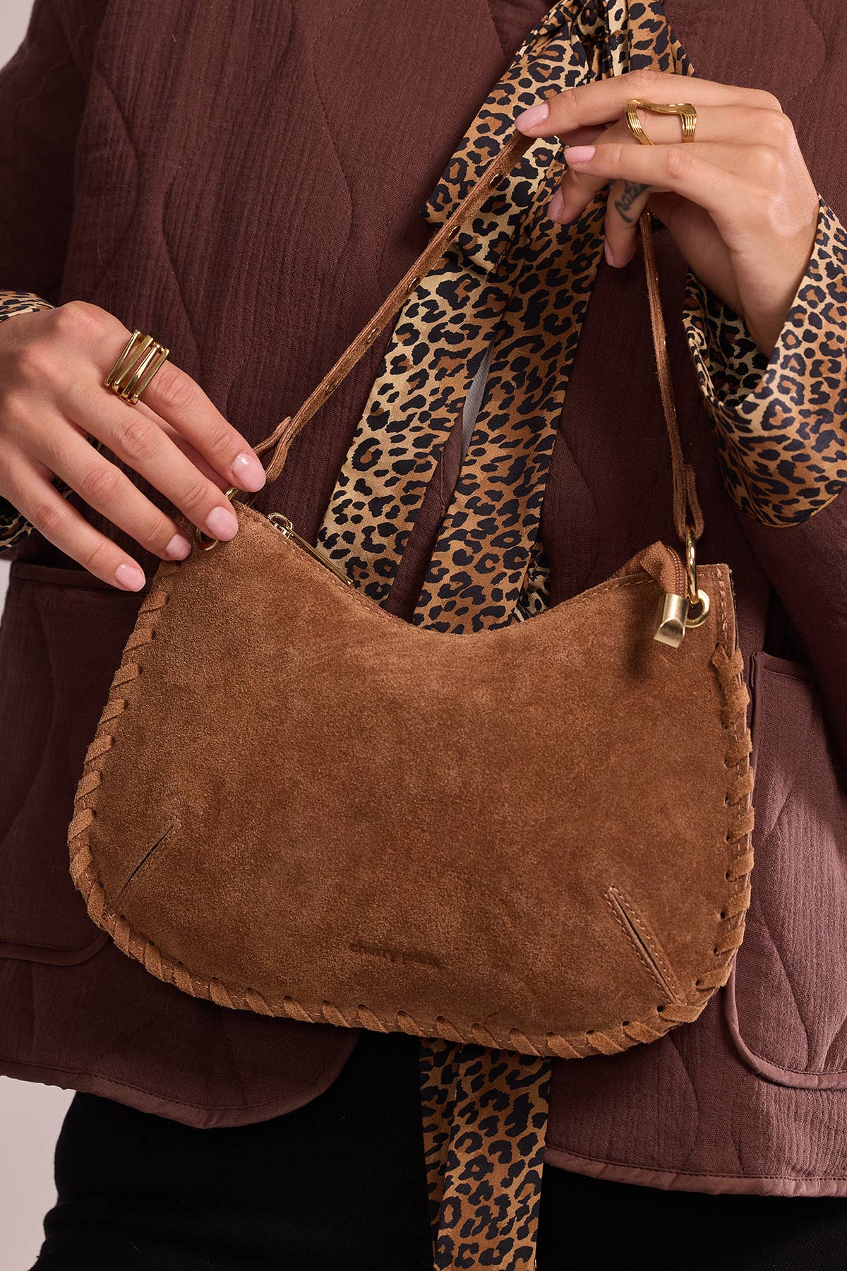 Close-up of the Joëlle camel suede bag showing its curved shape, stud accents, and piping trim.