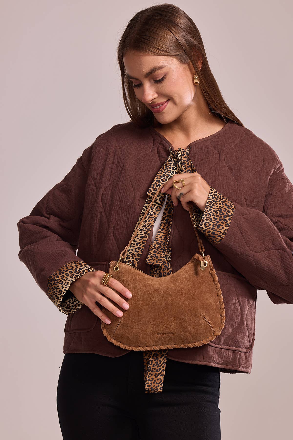 Model carrying the Joëlle camel suede bag by its short studded handle.