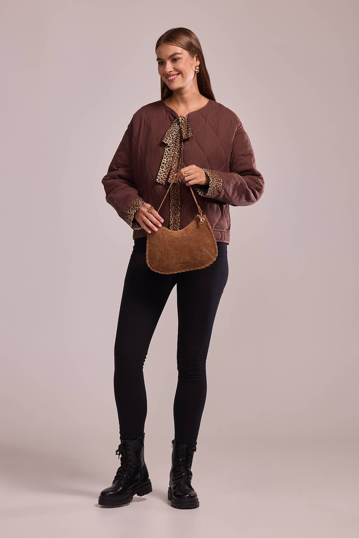 Full-length model styling the Joëlle camel suede handbag with a brown blouse and black pants.