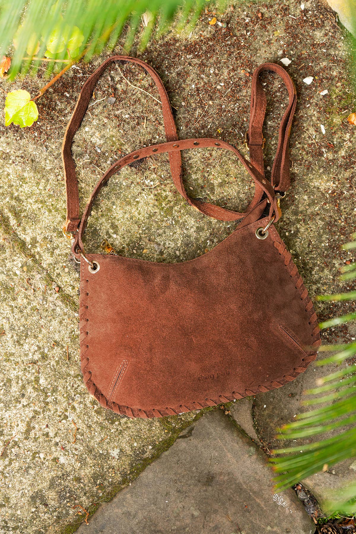 Brown Joelle Suede Bag styled outdoors on a stone surface with the shoulder strap attached.