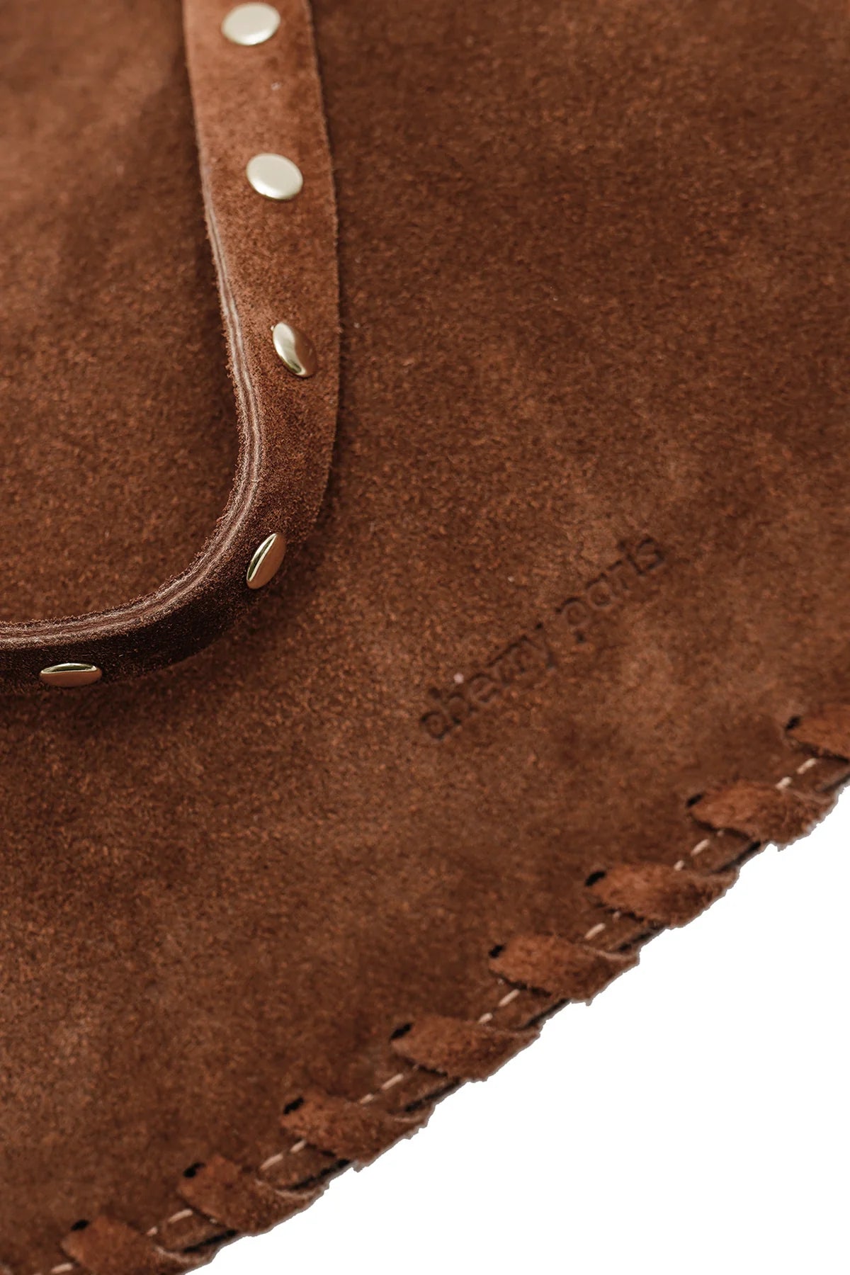 Close-up detail of the Joelle Suede Bag showing the brown suede texture, piping trim, stitching, and metallic studs.