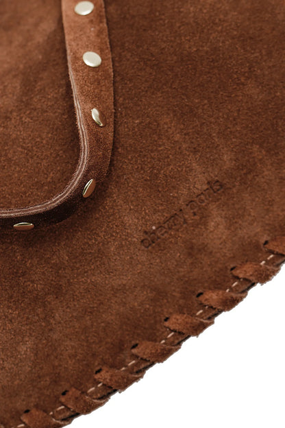 Close-up detail of the Joelle Suede Bag showing the brown suede texture, piping trim, stitching, and metallic studs.