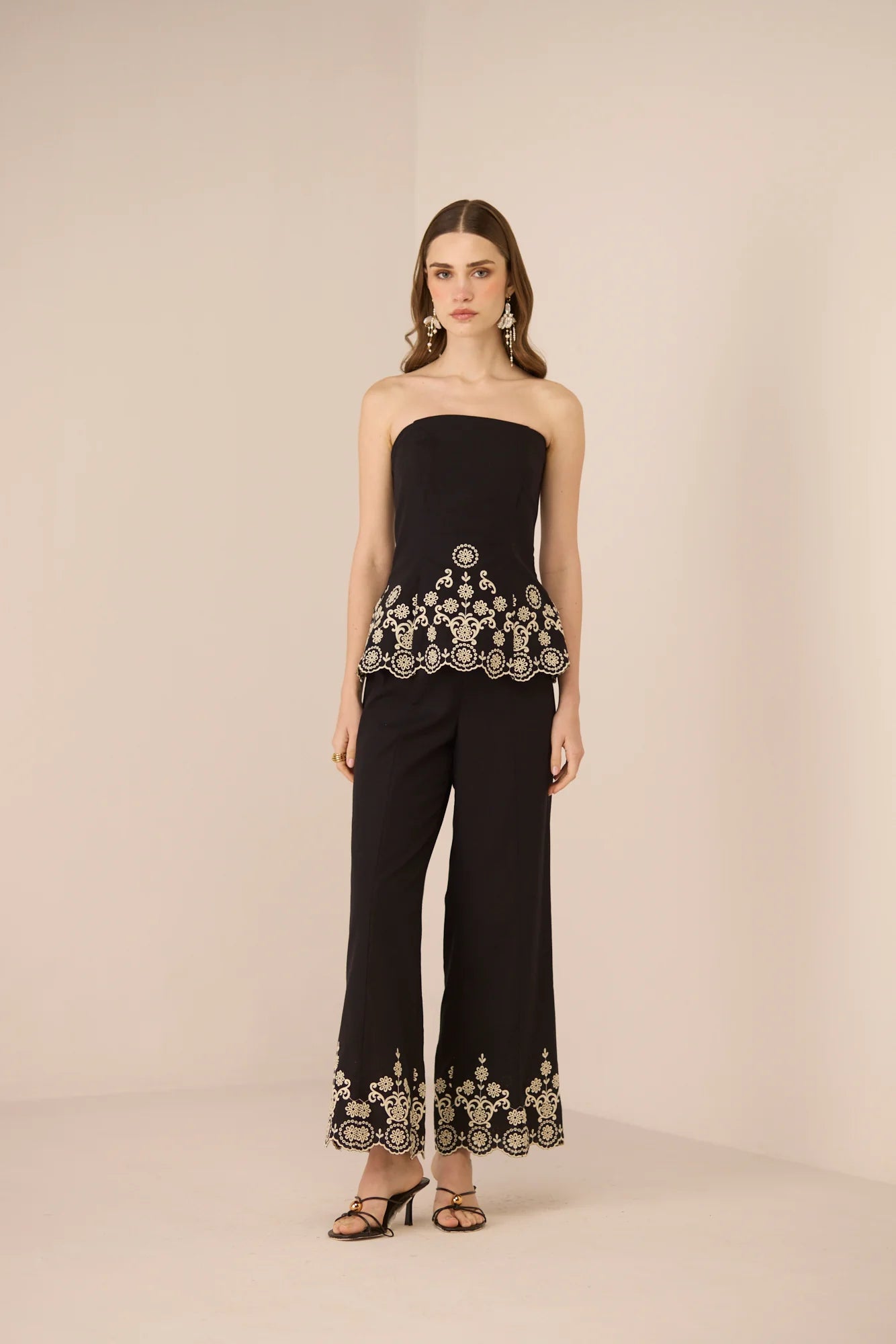 Angled front view of the Kaia Trousers in black with intricate contrast embroidery along the hem.