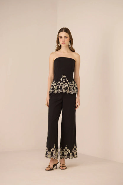 Angled front view of the Kaia Trousers in black with intricate contrast embroidery along the hem.