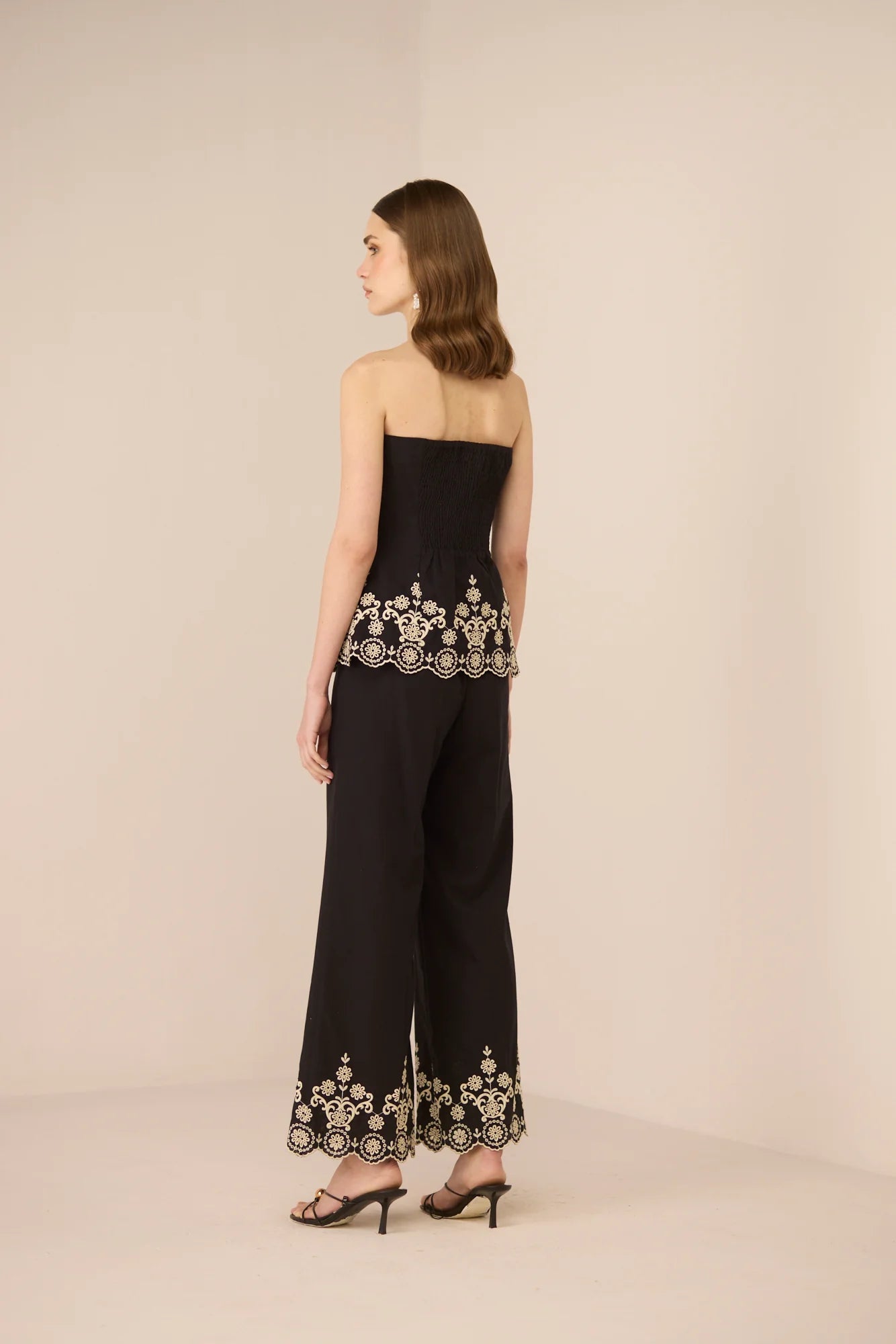 Back view of the Kaia Trousers in black, featuring embroidered scalloped hems and a clean straight-leg fit.