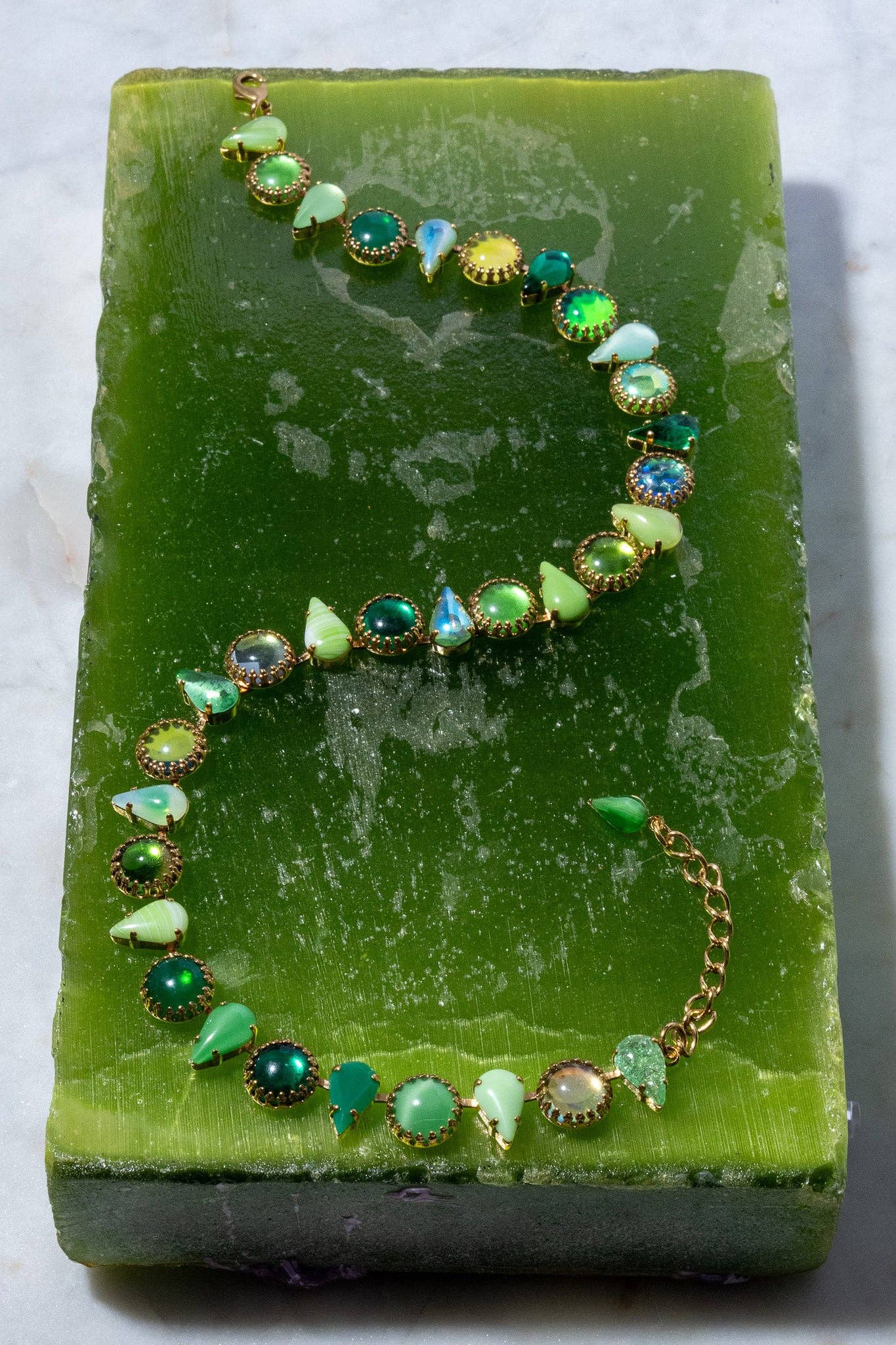 Full view of the Layering Choker in Salad Gold arranged on a green surface, featuring salad-green glass stones set in gold plate.