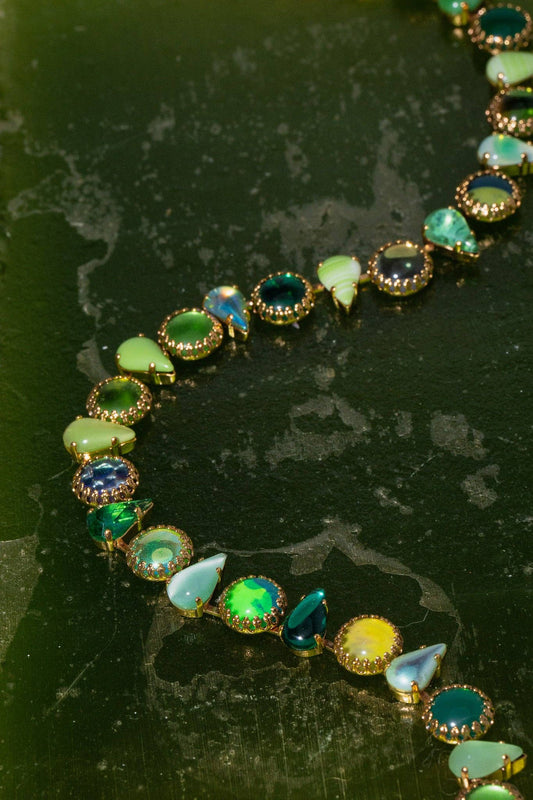 Layering Choker in Salad Gold featuring green vintage glass stones in round and fang shapes on a textured green background.