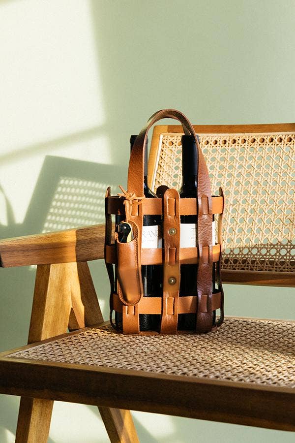 Woven full-grain leather wine tote with handles and wine key pouch styled on a woven chair in warm natural light.