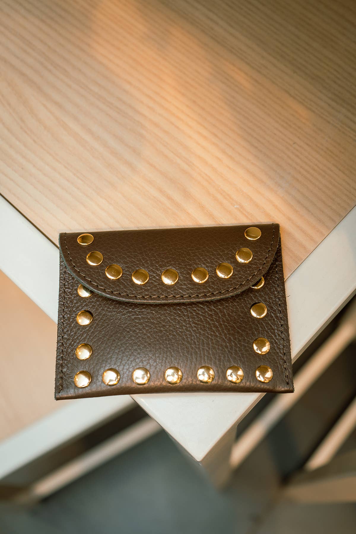 Leina Wallet in chocolate leather displayed on a wooden surface in a warm interior setting.
