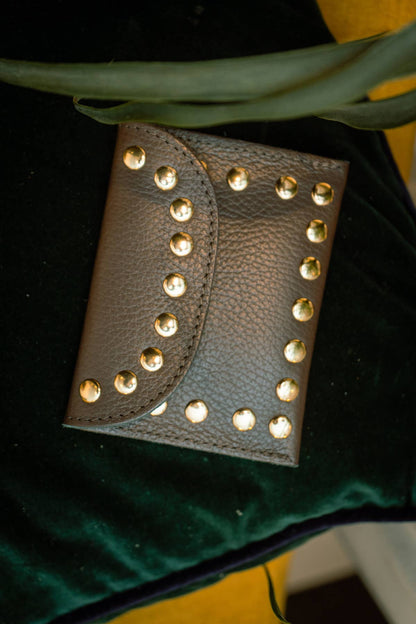 Chocolate leather Leina Wallet with gold-tone studs styled against dark green velvet.