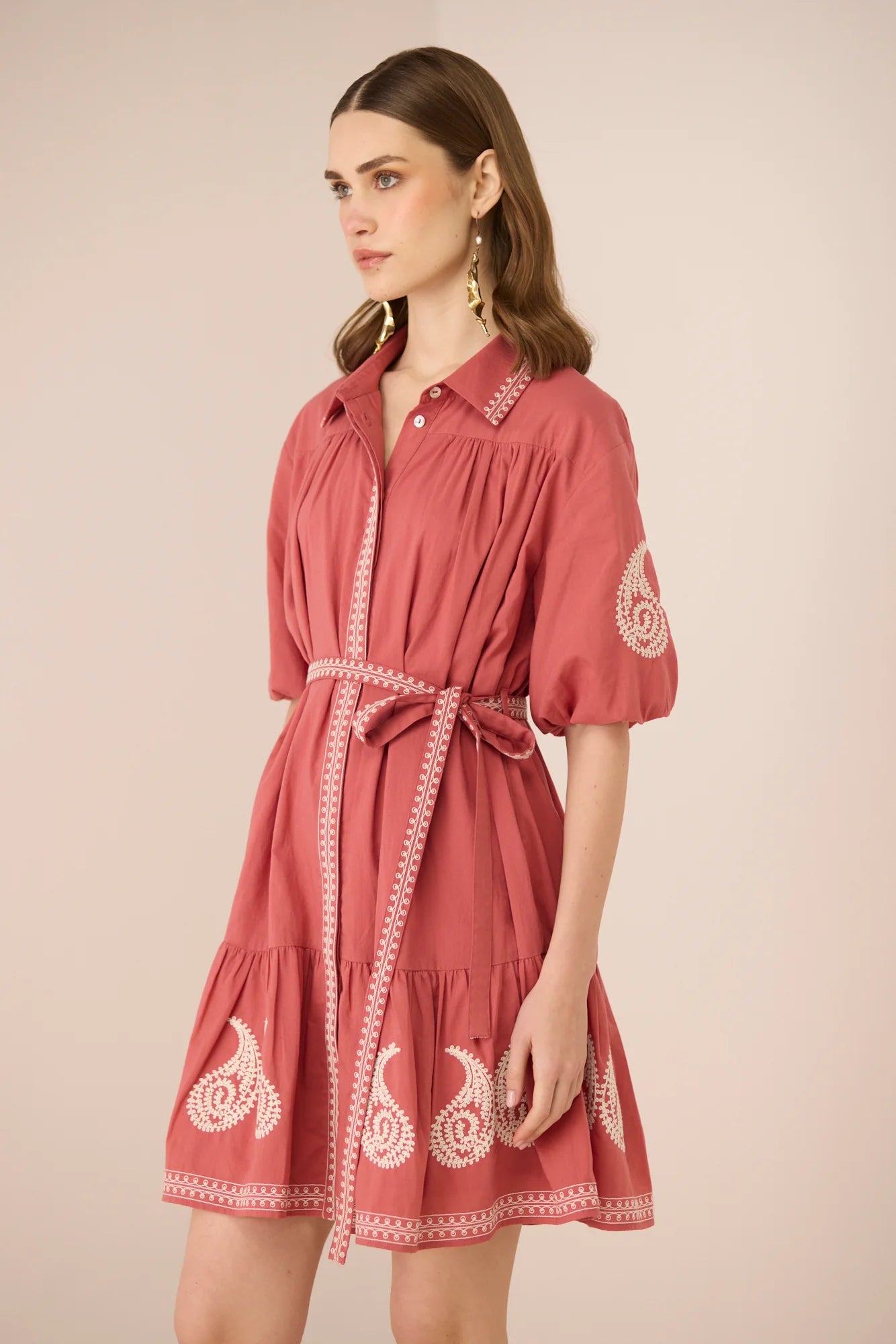 Angled front view of the Lizzie Mini Dress featuring a dusty rose mini silhouette, tie belt, and cream embroidered hem.