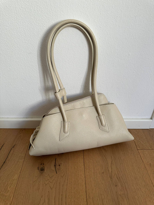 London Bag in beige pebbled leather with long tubular handles and an elongated geometric silhouette.