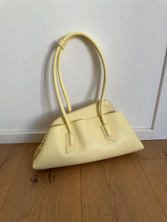 London Bag in pale butter yellow pebbled leather with long tubular handles and an elongated geometric silhouette.