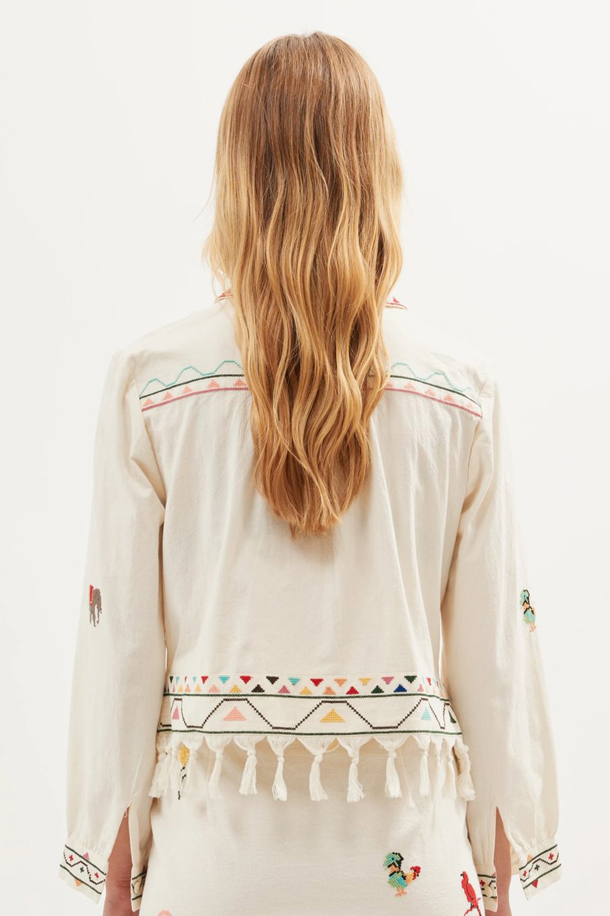 Back view of the Ludmilla Top in cream cotton with multicolor embroidered details, tassel fringe hem, and relaxed long sleeves