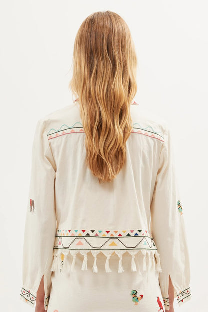 Back view of the Ludmilla Top in cream cotton with multicolor embroidered details, tassel fringe hem, and relaxed long sleeves