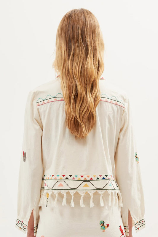 Back view of the Ludmilla Top in cream cotton with multicolor embroidered details, tassel fringe hem, and relaxed long sleeves