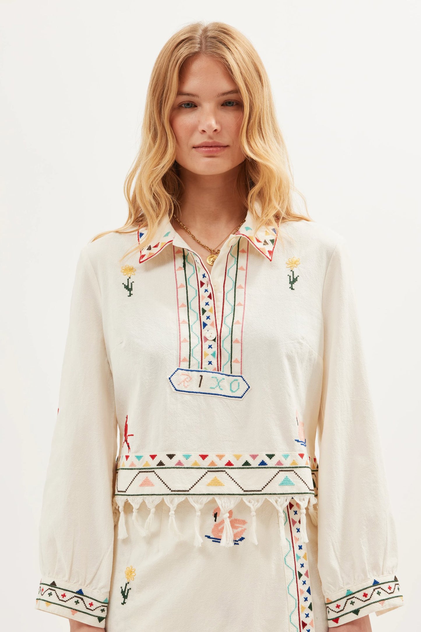 Model wearing the Ludmilla Top in Wildling Embroidery Cream featuring colorful embroidery, tassel fringe trim, long sleeves, and a relaxed cotton silhouette